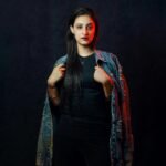 Stylish portrait of a young adult woman with a denim jacket and dark backdrop.