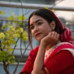 A thoughtful Indian woman in red traditional attire with nature in the background.